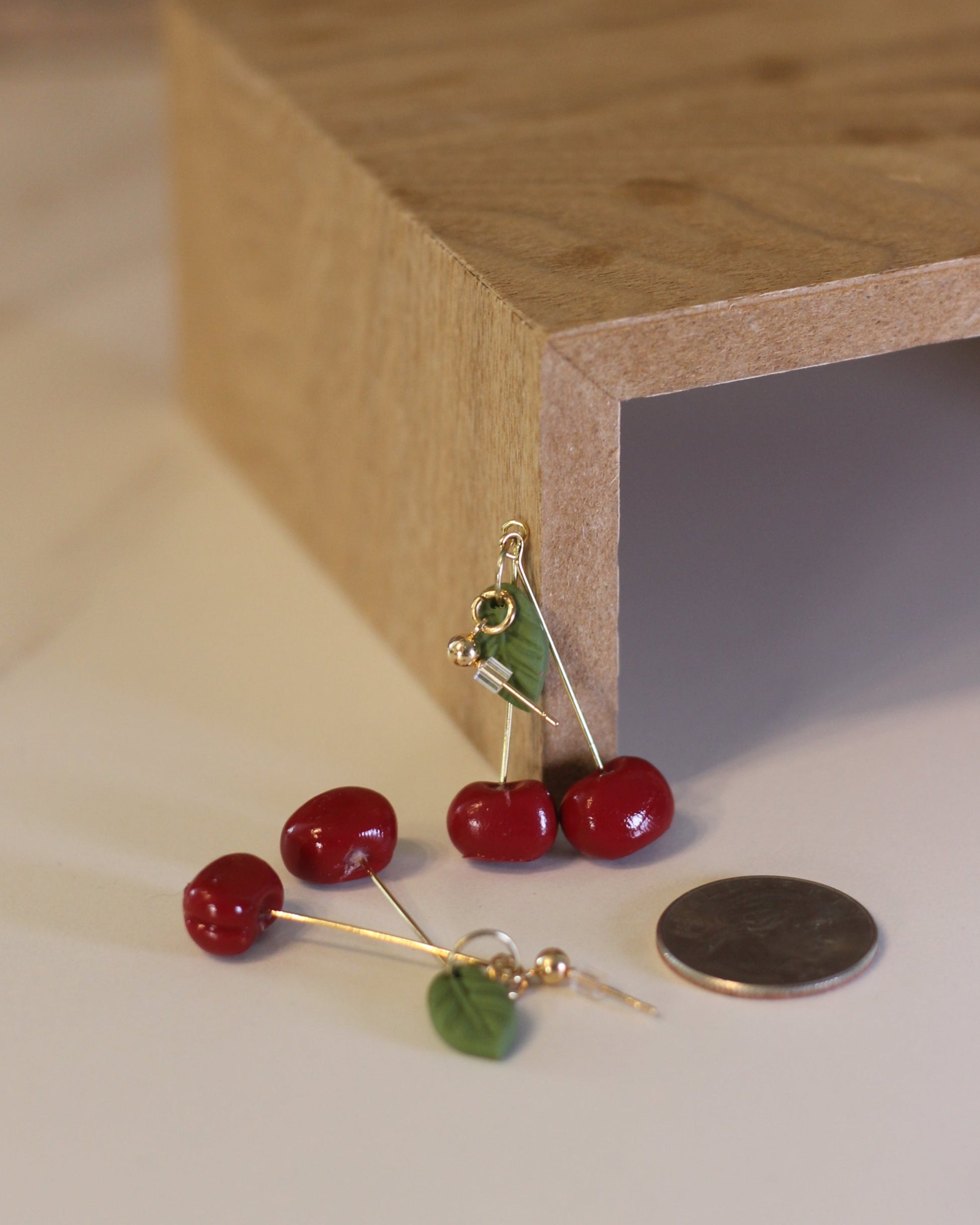 Close-up of a wooden frame with a coin and two cherry earrings on a white surface.